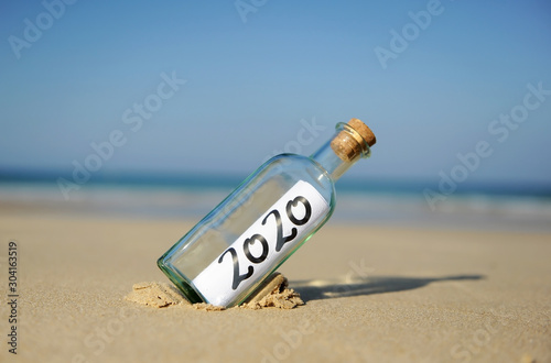 Happy New Year 2020 on the beach. Summer vacation concept. Message in a bottle found on the sand