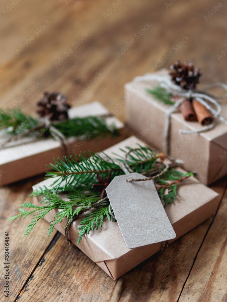 Christmas presents wrapped in craft paper with natural fir tree and thuja branches as decoration. Wooden table with hand made New Year gifts. Christmas presents wrapped in craft paper with natural fir tree and thuja branches as decoration. Wooden table with hand made New Year gifts.