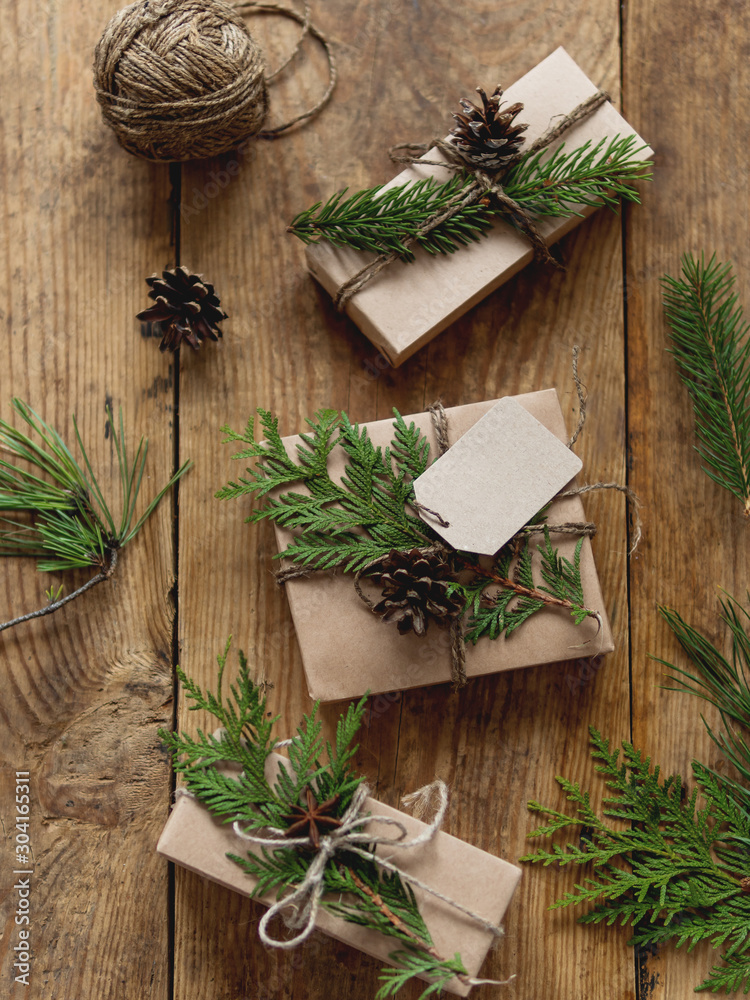 Christmas presents wrapped in craft paper with natural fir tree and thuja branches as decoration. Top view on wooden table with hand made New Year gifts. Christmas presents wrapped in craft paper with natural fir tree and thuja branches as decoration. Top view on wooden table with hand made New Year gifts.