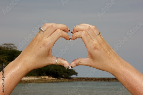 Female hand making a heart shape against a beautiful blue sky