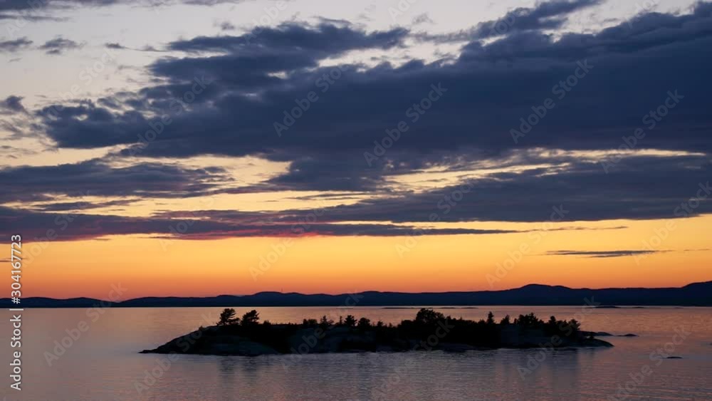 Beautiful Island Silhouette On The Calm Evening Waters Of Australia With Orange Sky, Clouds And Mountains In Background - Steady Shot Beautiful Island Silhouette On The Calm Evening Waters Of Australia With Orange Sky, Clouds And Mountains In Background - Steady Shot
