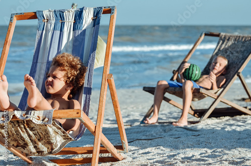 tanned baby boy resting and sunbathing in a deck chair on the sand by the blue s Fototapet