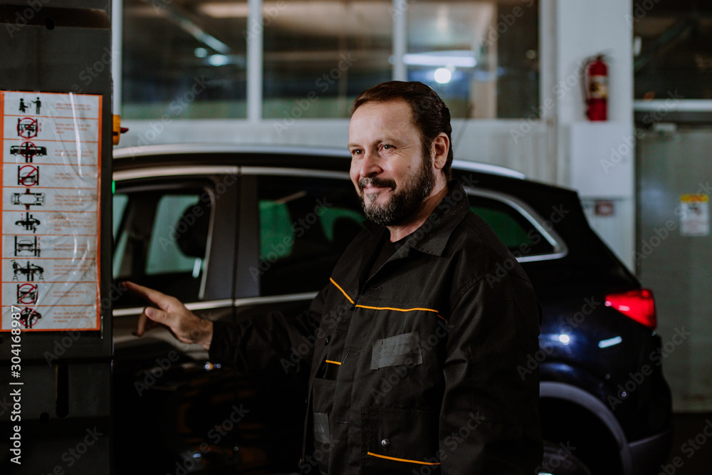 In the garage mechanic guy looking at the camera he is fixing the car and enjoying In the garage mechanic guy looking at the camera he is fixing the car and enjoying
