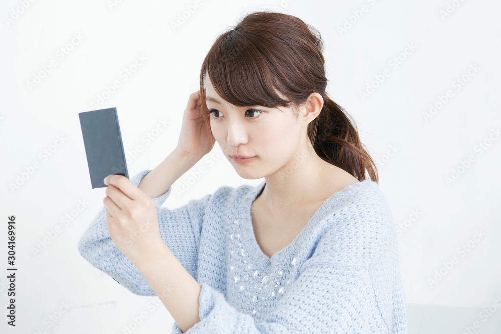 鏡を見て髪を整える女子大生