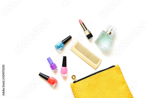 Colorful nail polishes, comb, pink lipstick and perfume. The contents of a yellow cosmetic bag. Flat lay beauty photography