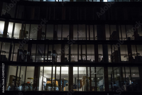 Facade of a business district building, a high rise, at night, in the evening, with only a few windows lit, and an employee alone working late in this office building.