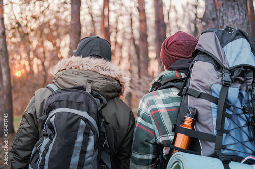 Active rest outdoors: two people with large backpacks look at the sunset in the forest. Getting away from the city and technology concept: backpackers enjoy the silence of the autumn nature