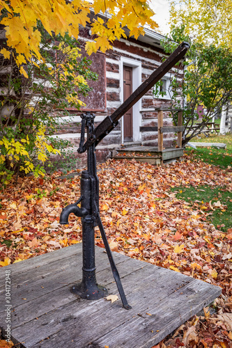 A black wrought iron old fashioned hand water pump outside a log cabin photo