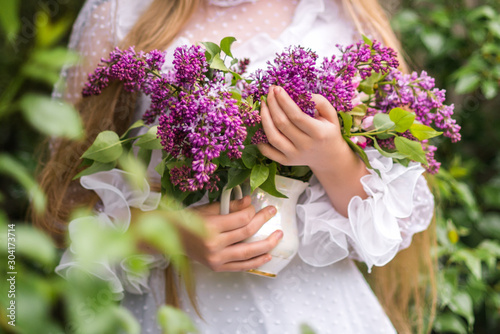 a young girl in a white dress holding a spring bouquet of lilacs on a background of greenery
