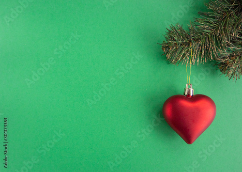 Christmas new year composition with heart red ball  and xmas tree on green background. greeting card. Flat lay, top view, copy space.