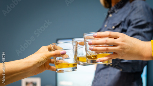 Close up on three female women hands holding a glasses of whiskey or brandy or cognac alcohol drink toasting celebrating at home