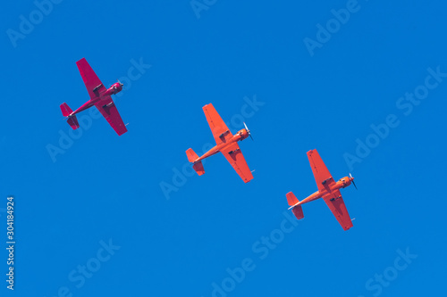 Three light-engine turboprop red aircraft fly in formation in a straight line in the sky.