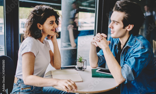 Caucasian couple enjoying live communication in cafeteria during leisure time togetherness  successful male and female hipsters looking each other in eyes and discussing startup in cafe interior