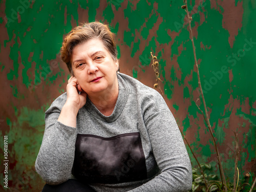 A thoughtful Mature plump woman walks the streets of the old city. On the background of the old green gate.