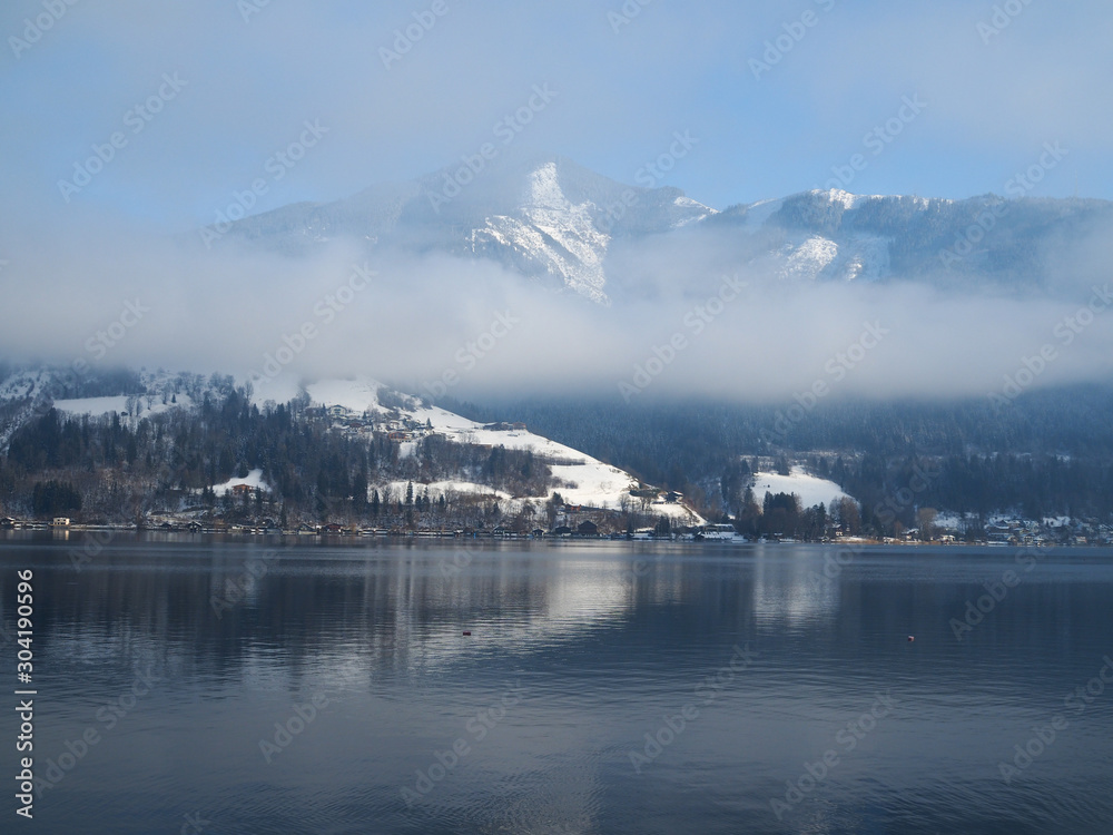 Wolkenverhangene schneebedeckte Berge am See im Winter, Zell am See, Österreich