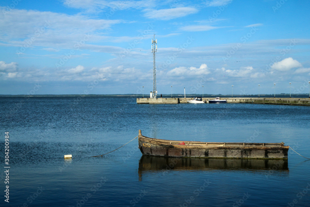 The calm sea shore in Lithuania in the town of Juodkranté. The fisherman´s boat floating by the pier.