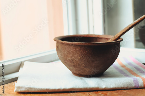 rustic flat lay, clay mortar with wooden pestle for grinding spices on linen background and string of onions on windowsill