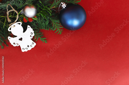spruce branches with Christmas balls of different colors and a wooden angel on a red background in the corner place for text. concept new year and Christmas