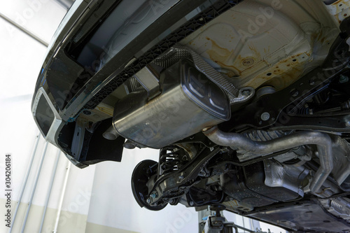 The rear muffler of a modern car and part of the exhaust system. The car is raised on a lift. Diagnostics and service of the car. Original spare parts for the car.