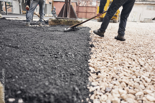 Laying new asphalt, covering the pit, on the rubble. Workers carry in shovels and using asphalt lute for smooth, hot asphalt.