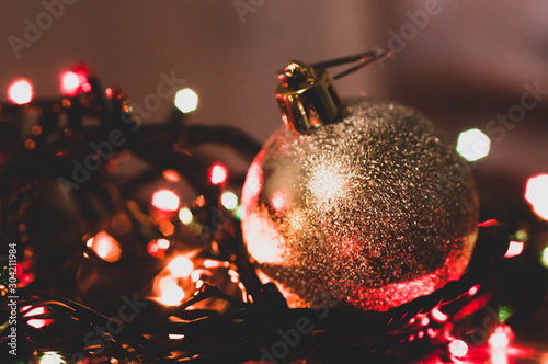 soft focus of golden shiny ball illuminated with multicolored blurred christmas lights in dark room