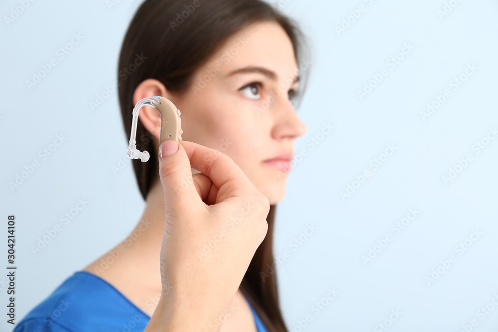Young woman and female hand with hearing aid on color background Young woman and female hand with hearing aid on color background