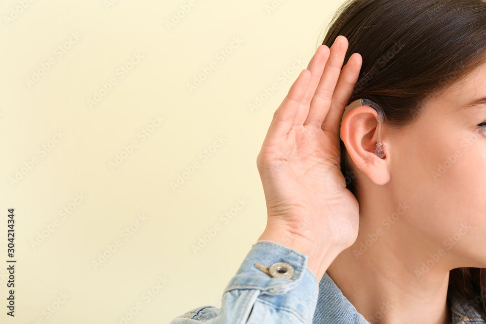 Fototapeta premium Young woman with hearing aid on color background