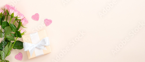 Pink roses, hearts and gift box on pastel beige background. Valentines day banner template, Mother day card mockup. Flat lay, top view, copy space.