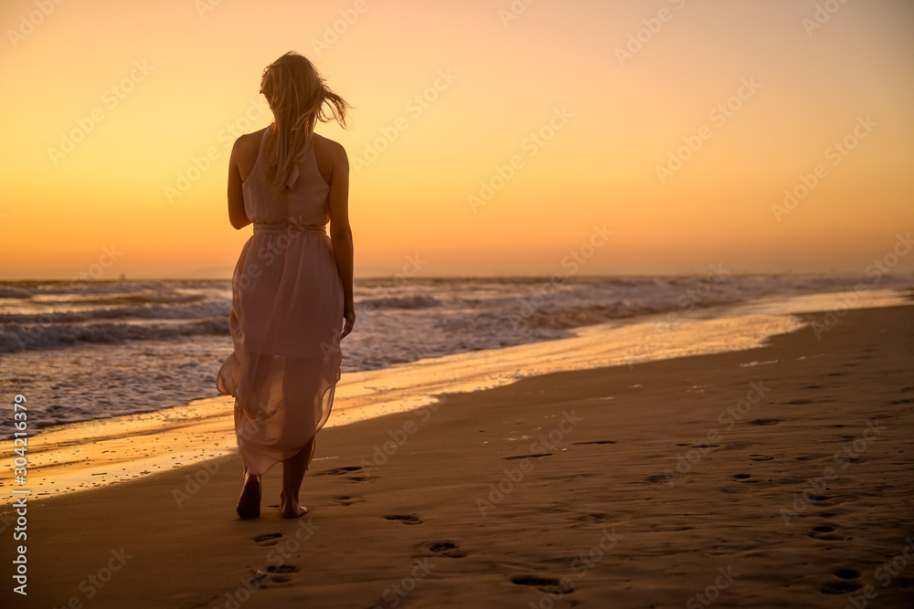 Beautiful woman wearing a gorgeous summer clothes and walking away into the sunset somewhere on the southern coast of the Pacific Ocean