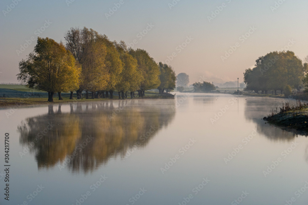 Mirror-like river with reflections of trees in autumn colors Mirror-like river with reflections of trees in autumn colors