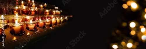 Fototapeta Candles in a church, cathedral or temple, in yellow transparent candlesticks
