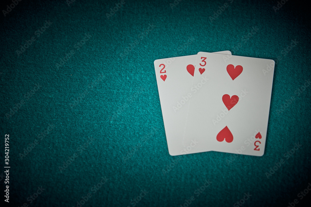 Cards of two and three from hearts on a green poker game mat. Superior view.