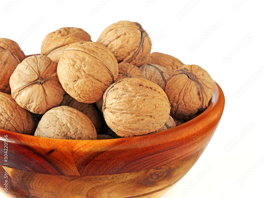 Whole walnuts in shell in wooden bowl over white background Whole walnuts in shell in wooden bowl over white background