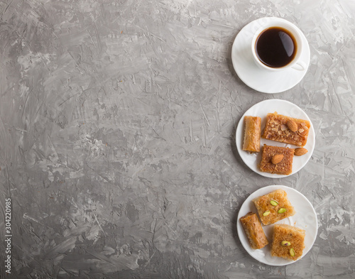 traditional arabic sweets on white plate and a cup of coffee on a gray concrete background.  top view, copy space.