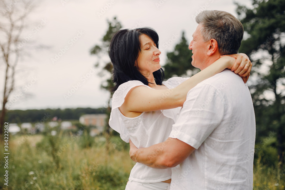 Adult couple in a summer field. Handsome senior in a white shirt. Woman in a white blouse