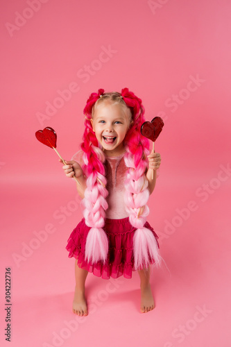 little girl with braids of pink kanekalon holds a heart-shaped Lollipop on a pink background. refusal of sweets. the concept of Valentine s day