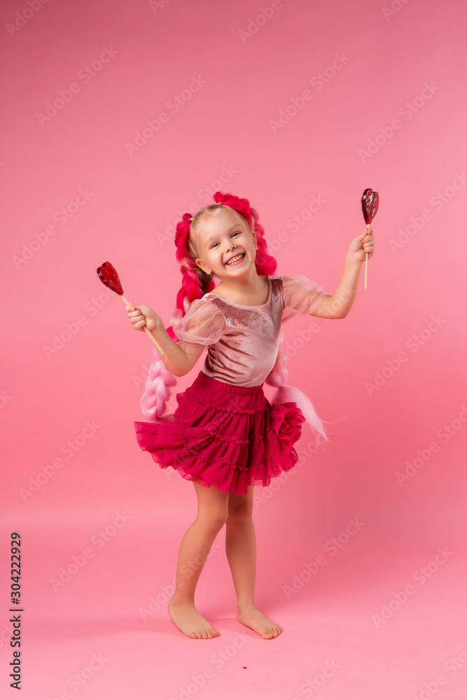 little girl with braids of pink kanekalon holds a heart-shaped Lollipop on a pink background. refusal of sweets. the concept of Valentine's day