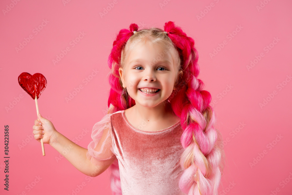 little girl with braids of pink kanekalon holds a heart-shaped Lollipop on a pink background. refusal of sweets. the concept of Valentine's day
