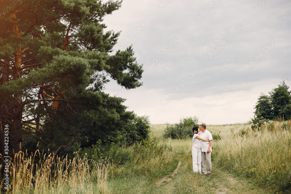 Adult couple in a summer field. Handsome senior in a white shirt. Woman in a white blouse Adult couple in a summer field. Handsome senior in a white shirt. Woman in a white blouse