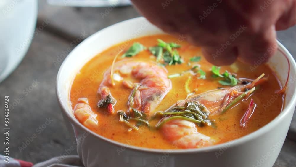 Someone pouring coriander on Spicy Soup with Prawn in a bowl. Tom Yum Goong. Thai food.