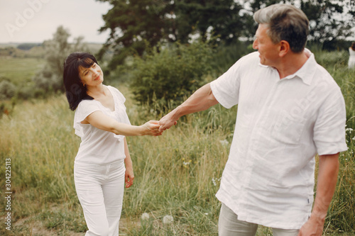 Adult couple in a summer field. Handsome senior in a white shirt. Woman in a white blouse © hetmanstock2