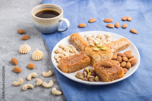 traditional arabic sweets (basbus, kunafa, baklava), a cup of coffee and nuts on a gray concrete background side view, close up.
