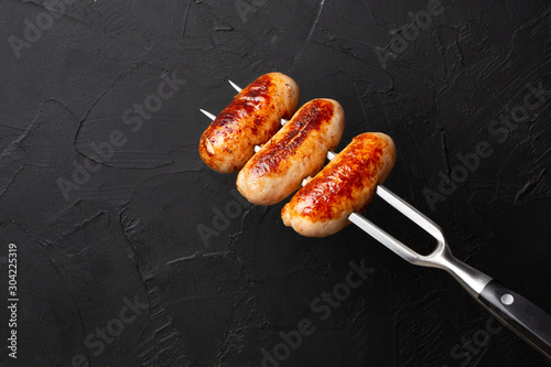fried chicken sausages on a large meat fork on black background
