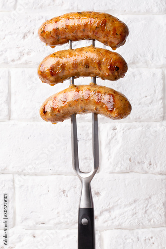 fried chicken sausages on a large meat fork on white background