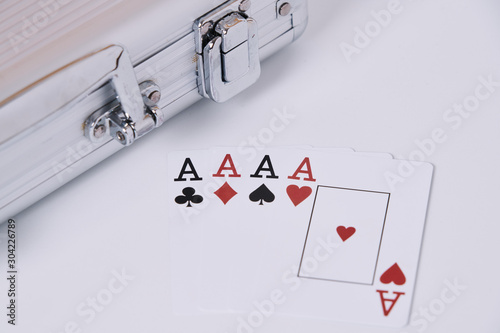 Game cards. Four cards, four aces, four symbols in background and white table and poker chips briefcase in the frame.