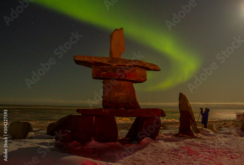 Northern lights and inukshuk with tourist photo