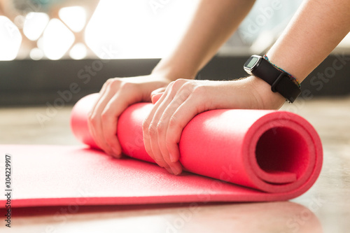 Stock photo of a young woman rolling the mat after exercising at home in the living room