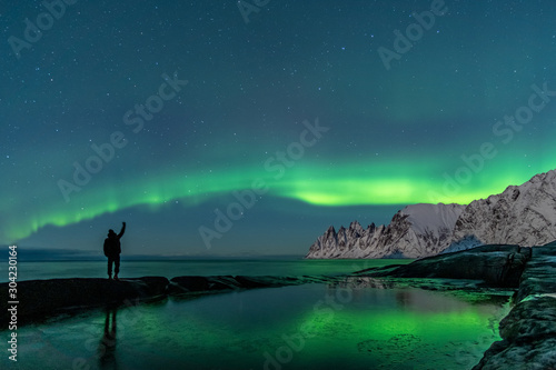 Man watching the northern lights  Aurora Borealis  Devil Teeth mountains in the background  Tungeneset  Senja  Norway