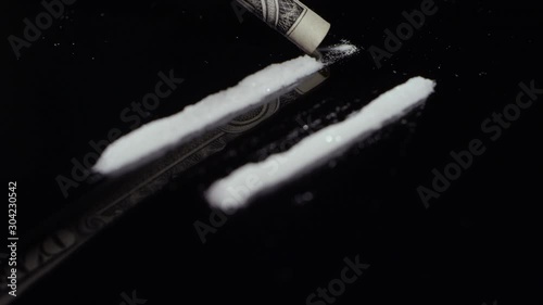 Rack focus of cocaine getting snorted up with a dollar bill on a mirrored surface 