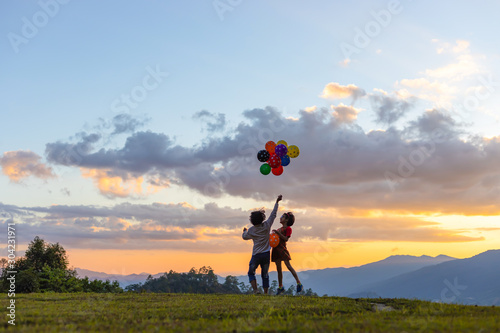 Two sister children playing with colored balloons at sunset.
